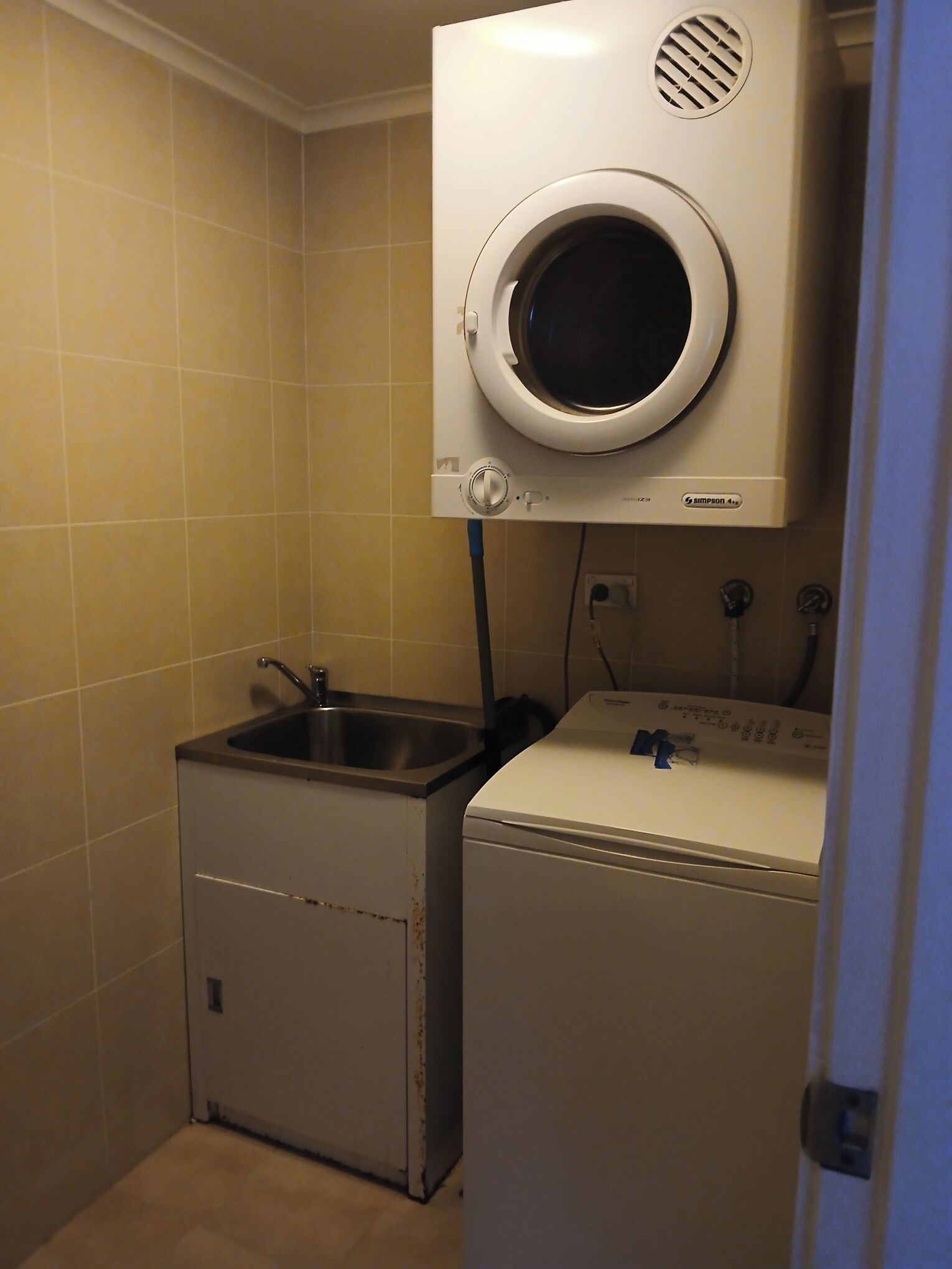 A compact laundry area with a front-loading washer and dryer, a sink, and tiled walls.