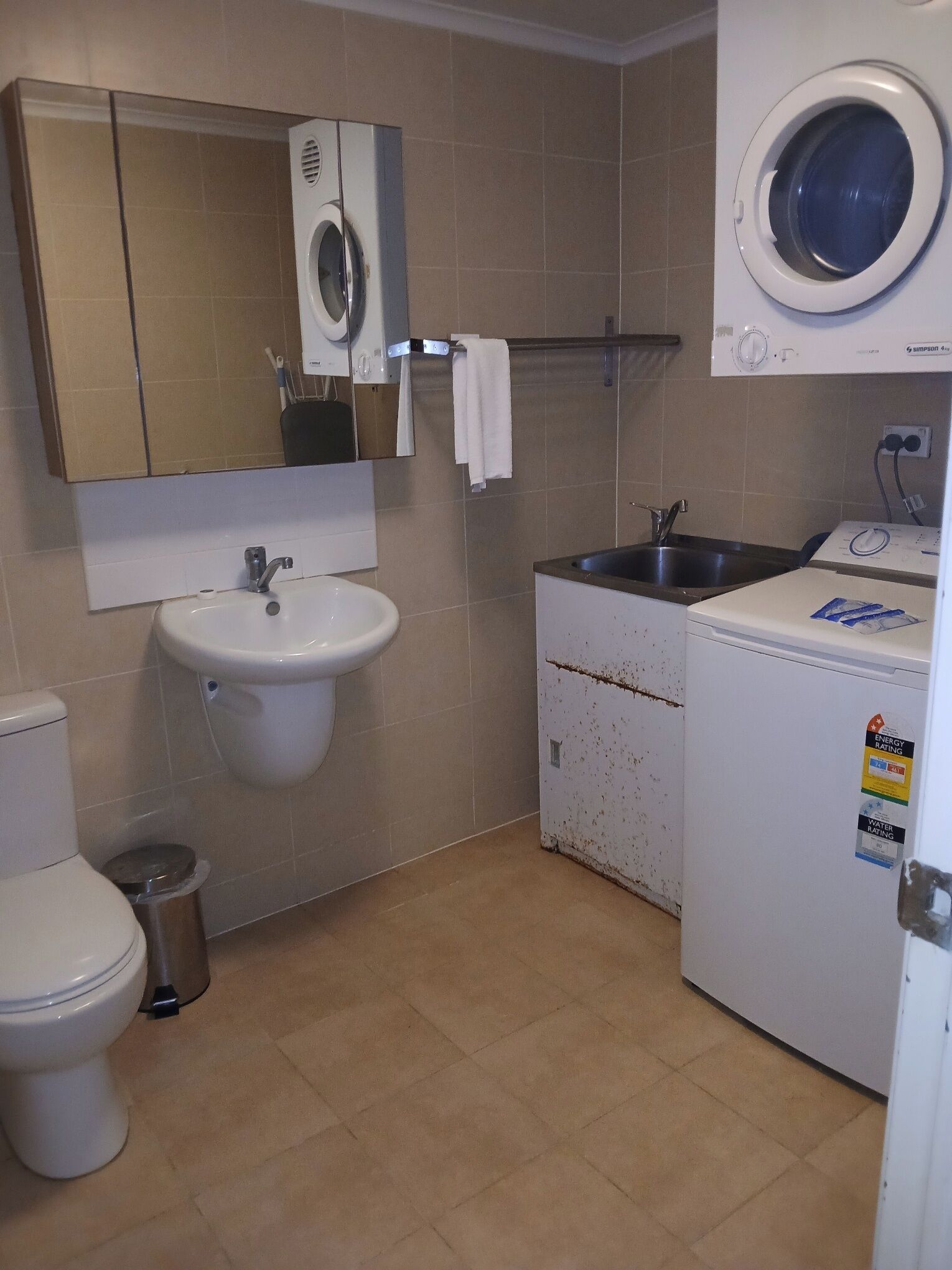 A small bathroom with a sink, toilet, mirror, and a washing machine.