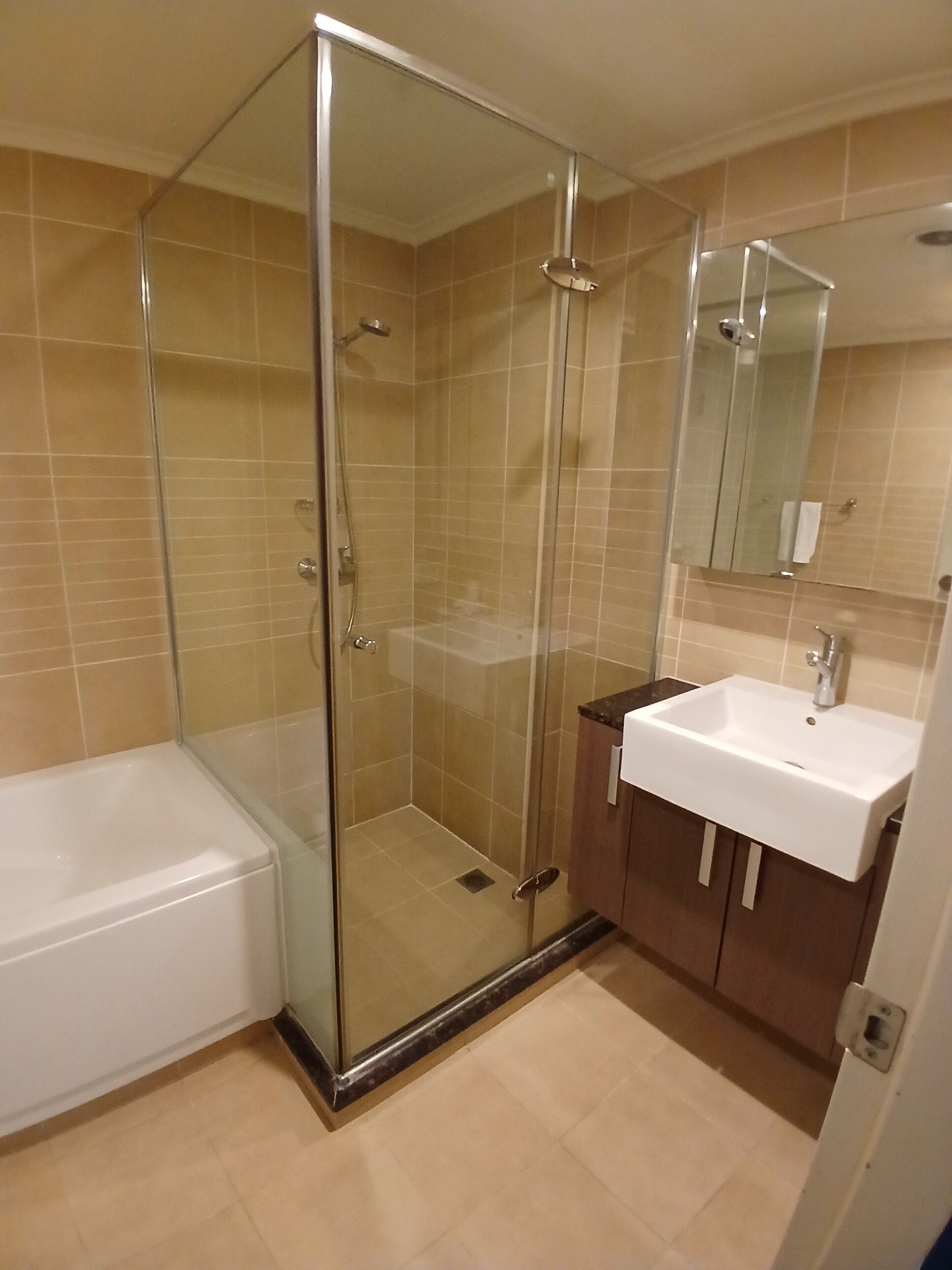 A bathroom with a glass-enclosed shower, a white bathtub, and a wooden vanity with a sink.