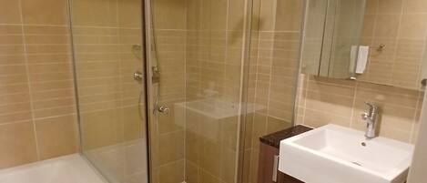 A bathroom with a glass-enclosed shower, a white bathtub, and a wooden vanity with a sink.