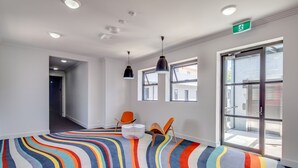 A brightly lit room with a colorful striped carpet, two chairs, a white ottoman, and a large window with a view of buildings outside. - The Star Apartments (Newcastle West)