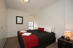 A hotel room with a bed, a nightstand, a lamp, and a window with blinds. - The Star Apartments (Newcastle West)