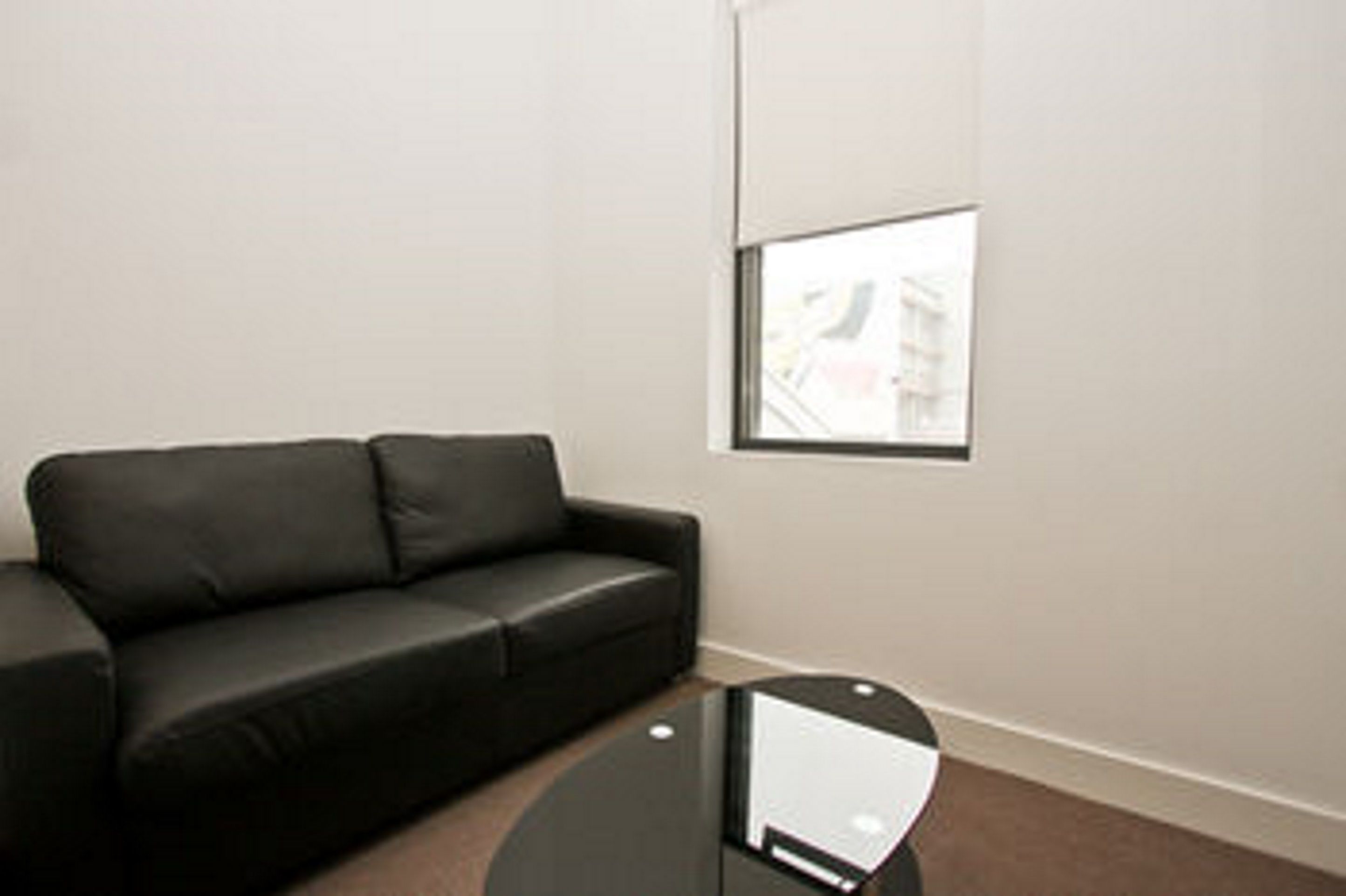 A room with a black leather sofa, a small black table, and a window with a view of buildings.