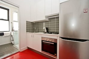 A compact kitchen with white cabinets, a stainless steel refrigerator, a built-in oven, and a tiled backsplash. - The Star Apartments (Newcastle West)