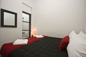 A bedroom with a bed, a red and white pillow, a red blanket, a white towel, and a nightstand with a lamp. - The Star Apartments (Newcastle West)