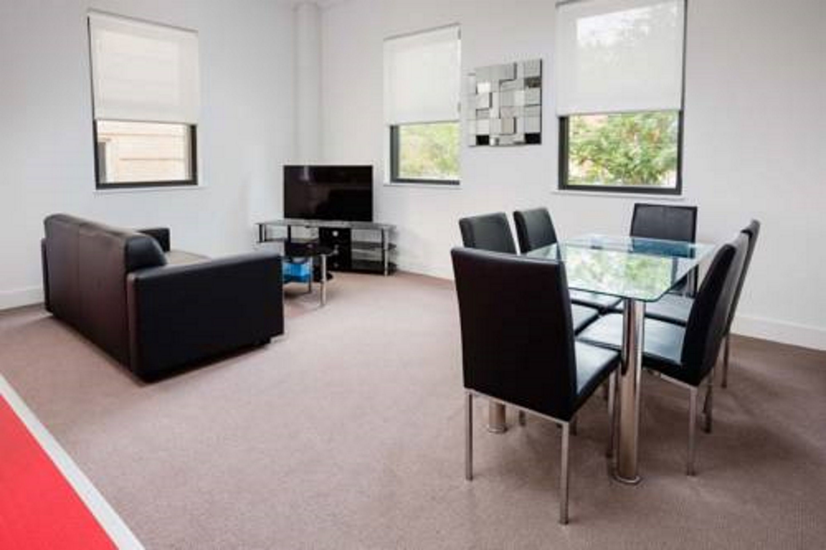 A modern living room with a glass dining table, black chairs, a sofa, a TV, and a coffee table.