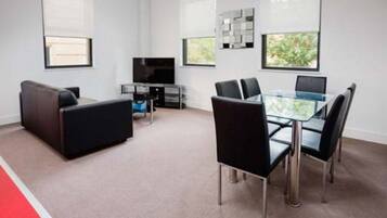 A modern living room with a glass dining table, black chairs, a sofa, a TV, and a coffee table.