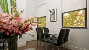 A modern dining area with a glass table and black chairs, a vase of pink flowers, and a framed picture on the wall. - The Star Apartments (Newcastle West)