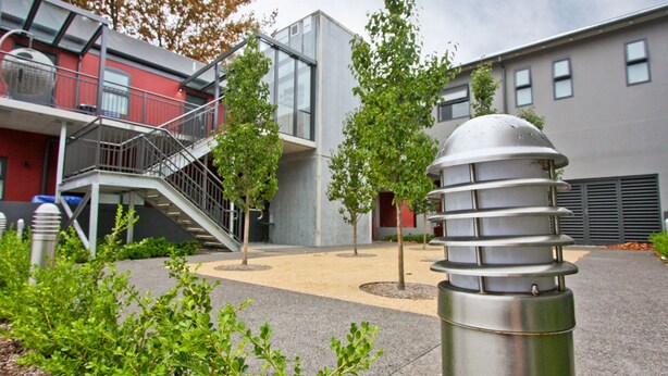 A modern building with a staircase leading to a balcony, surrounded by trees and a metal structure. - The Star Apartments (Newcastle West)