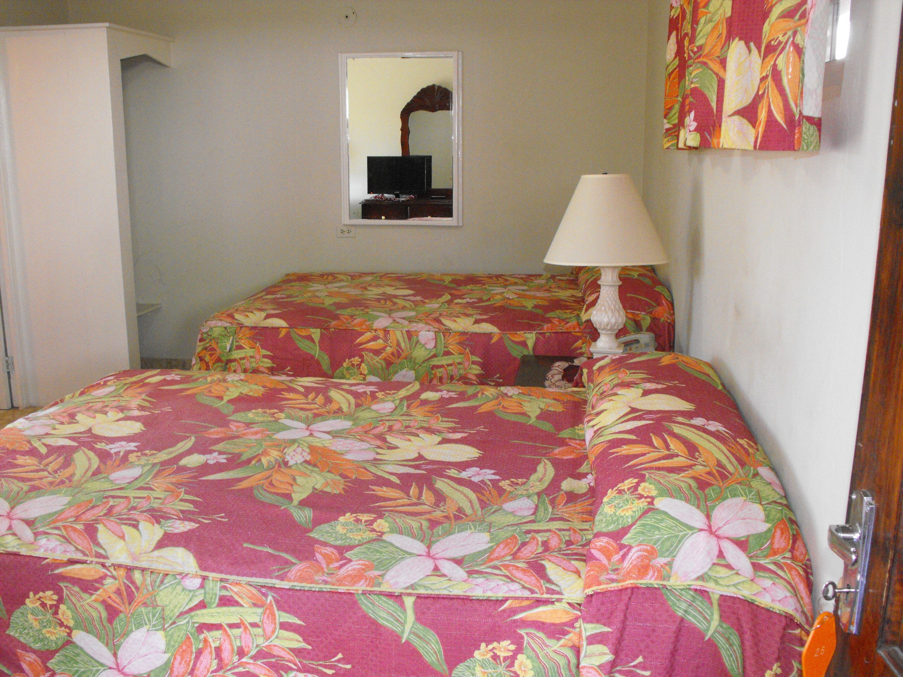 A hotel room with a bed covered in floral bedding, a bedside lamp, and a mirror on the wall.