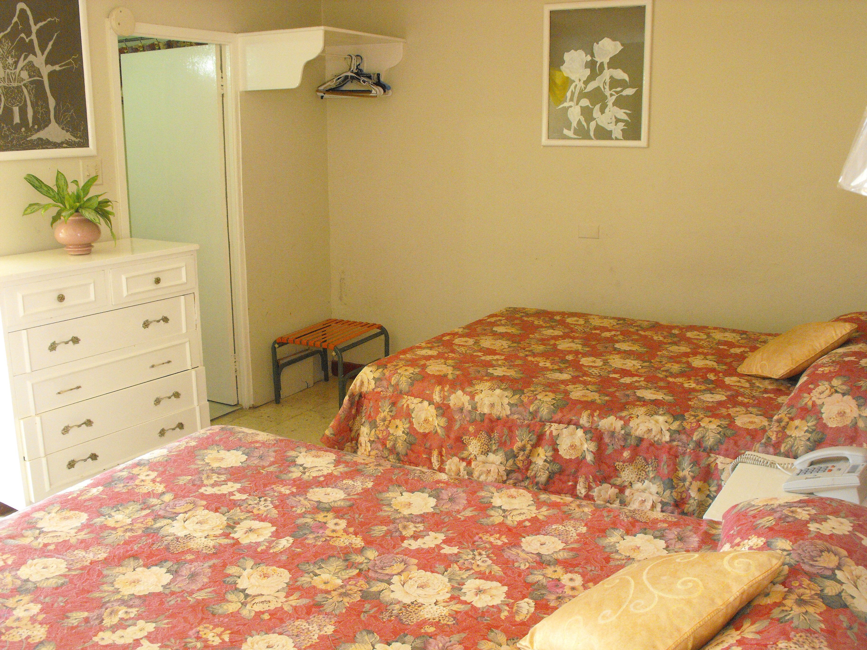 A bedroom with two beds, a dresser, a small table, and a hanging light fixture.