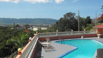 Una piscina de borde curvo, rodeada por una barandilla blanca y un muro rojo.