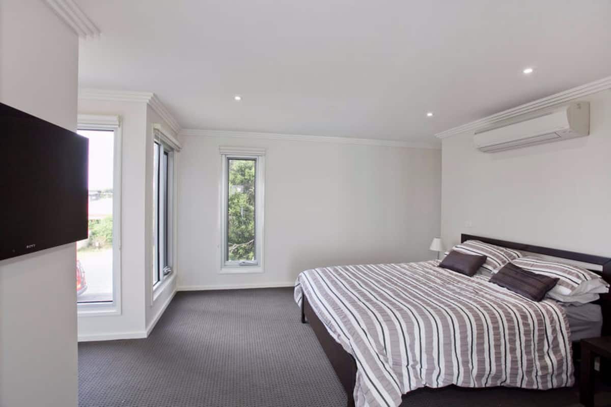 A bedroom with a large bed, a television, a window, and an air conditioning unit.