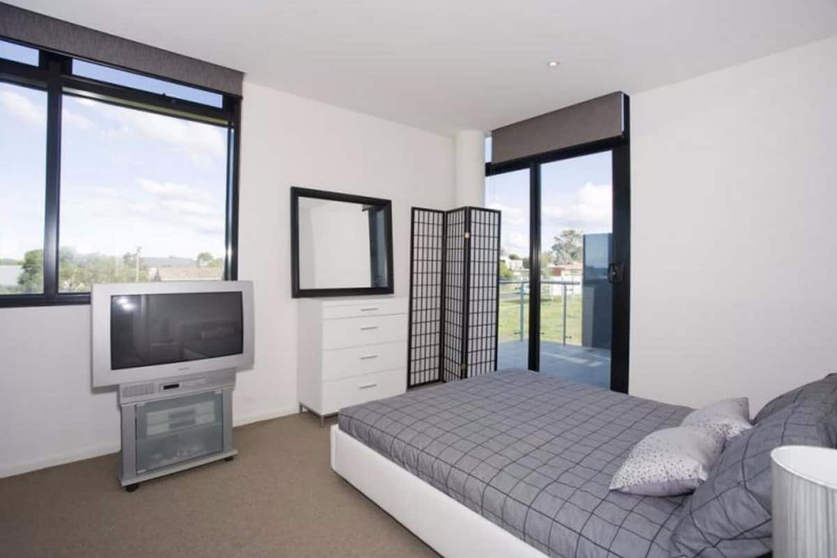 A modern bedroom with a large bed, a television, a dresser, and a sliding glass door leading to a balcony.