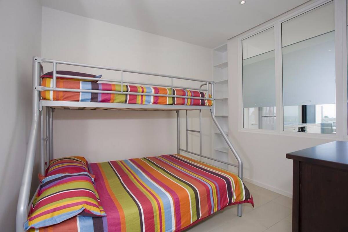 A bunk bed with colorful bedding, a desk, and a window with blinds.