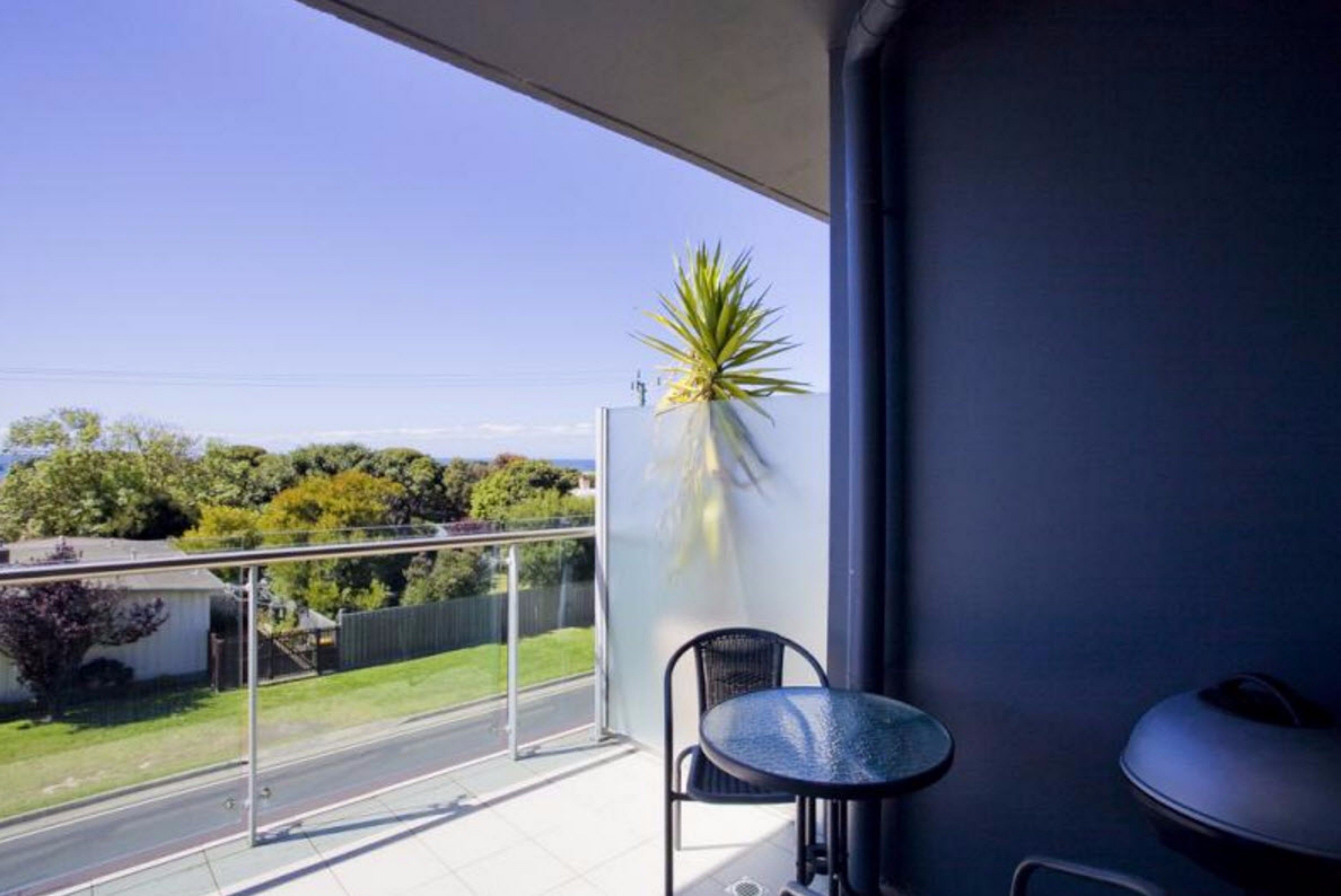 A balcony with a glass door, a small round table, a chair, and a potted plant.