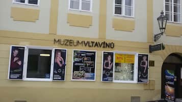 A building with the sign "MUZEUMMVLTAVINU" indicating a museum. There are multiple posters advertising the museum's exhibits and a seasonal clearance sale.