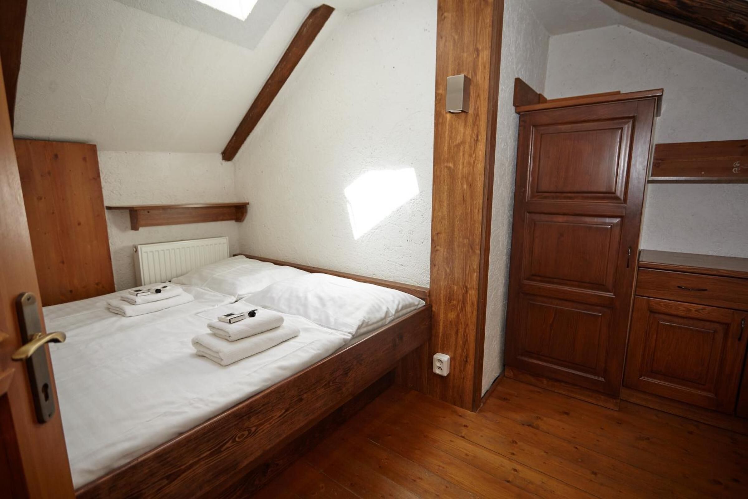 A small, cozy bedroom with a wooden bed, a built-in wardrobe, and a sloped ceiling.