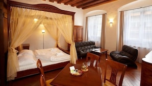A hotel room with a large bed, a sitting area with a leather sofa, a dining table, and a small table with a basket of snacks. - Residence Muzeum Vltavinu (Cesky Krumlov)