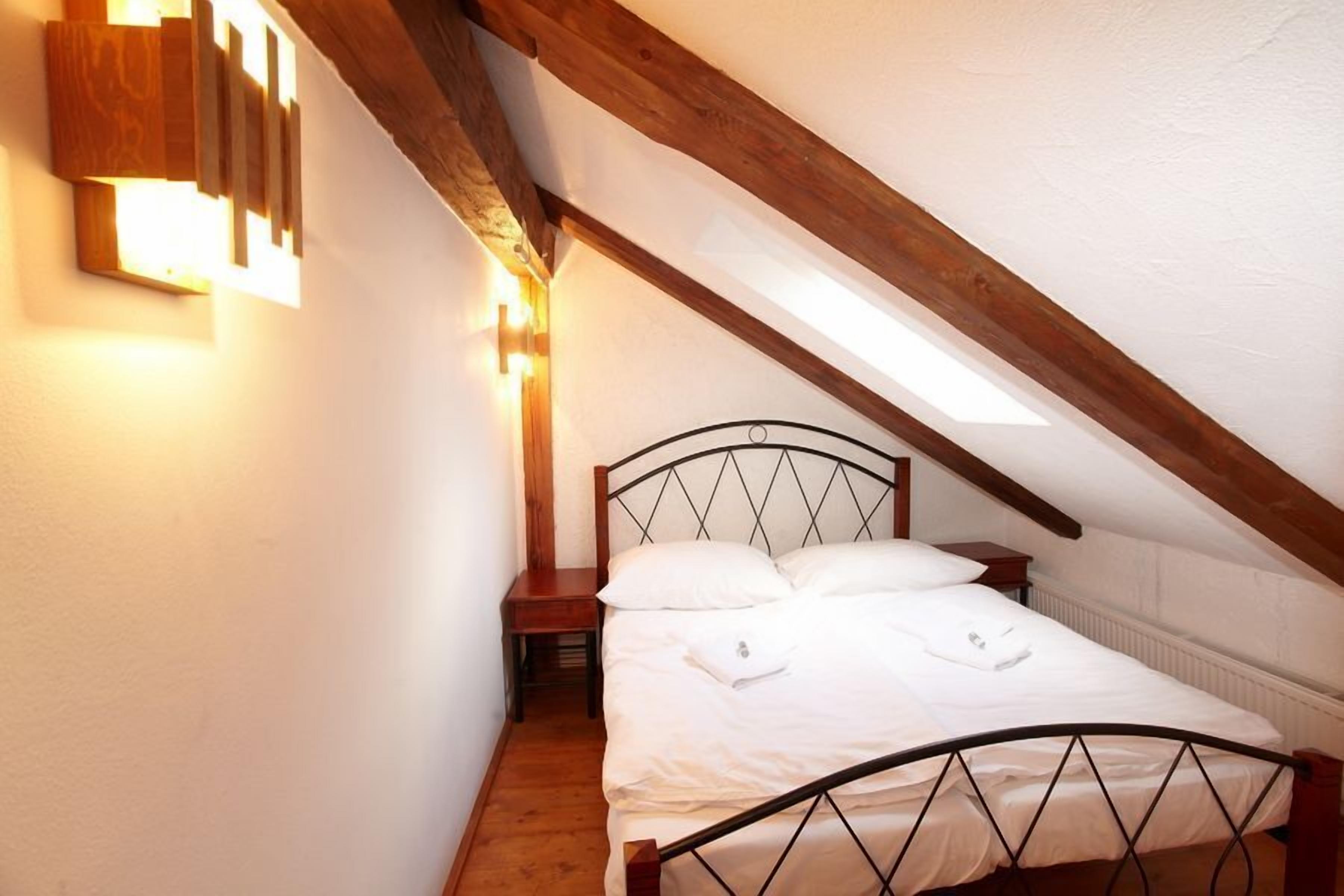 Une chambre avec un plafond en pente, un lit avec une literie blanche, une table de chevet et un luminaire fixé au mur.
