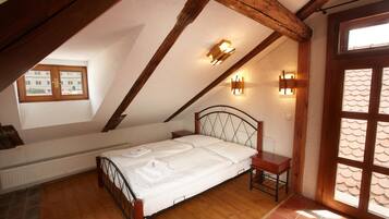 A bedroom with a sloped ceiling, wooden beams, a bed with white linens, two bedside tables, and a window with a view of buildings.