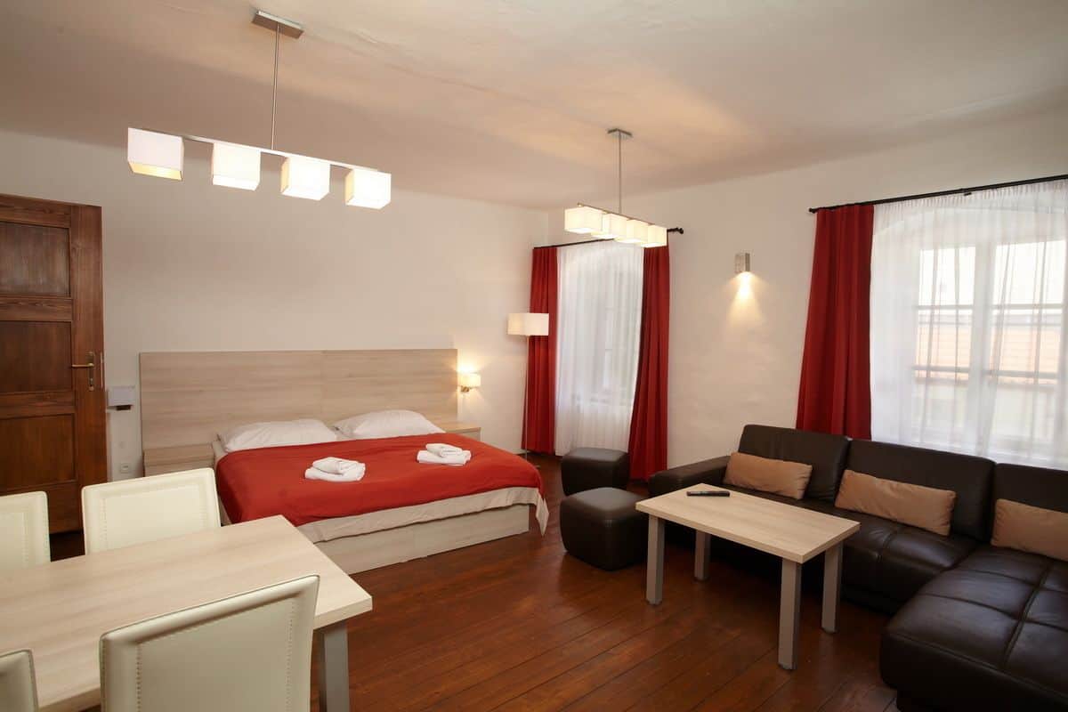 A hotel room with a bed, a sofa, a table, and a desk. There are curtains and a window.