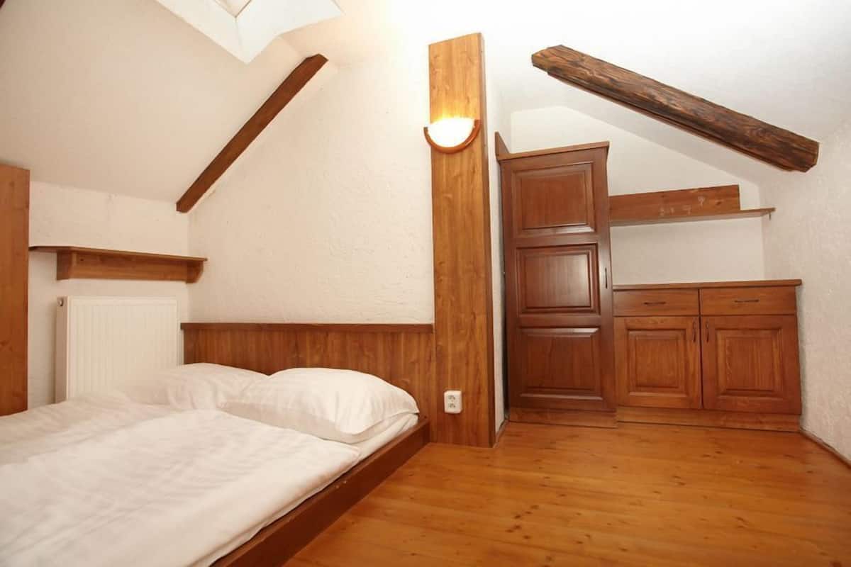 A bedroom with a wooden bed, a built-in wardrobe, and a sloped ceiling with exposed beams.