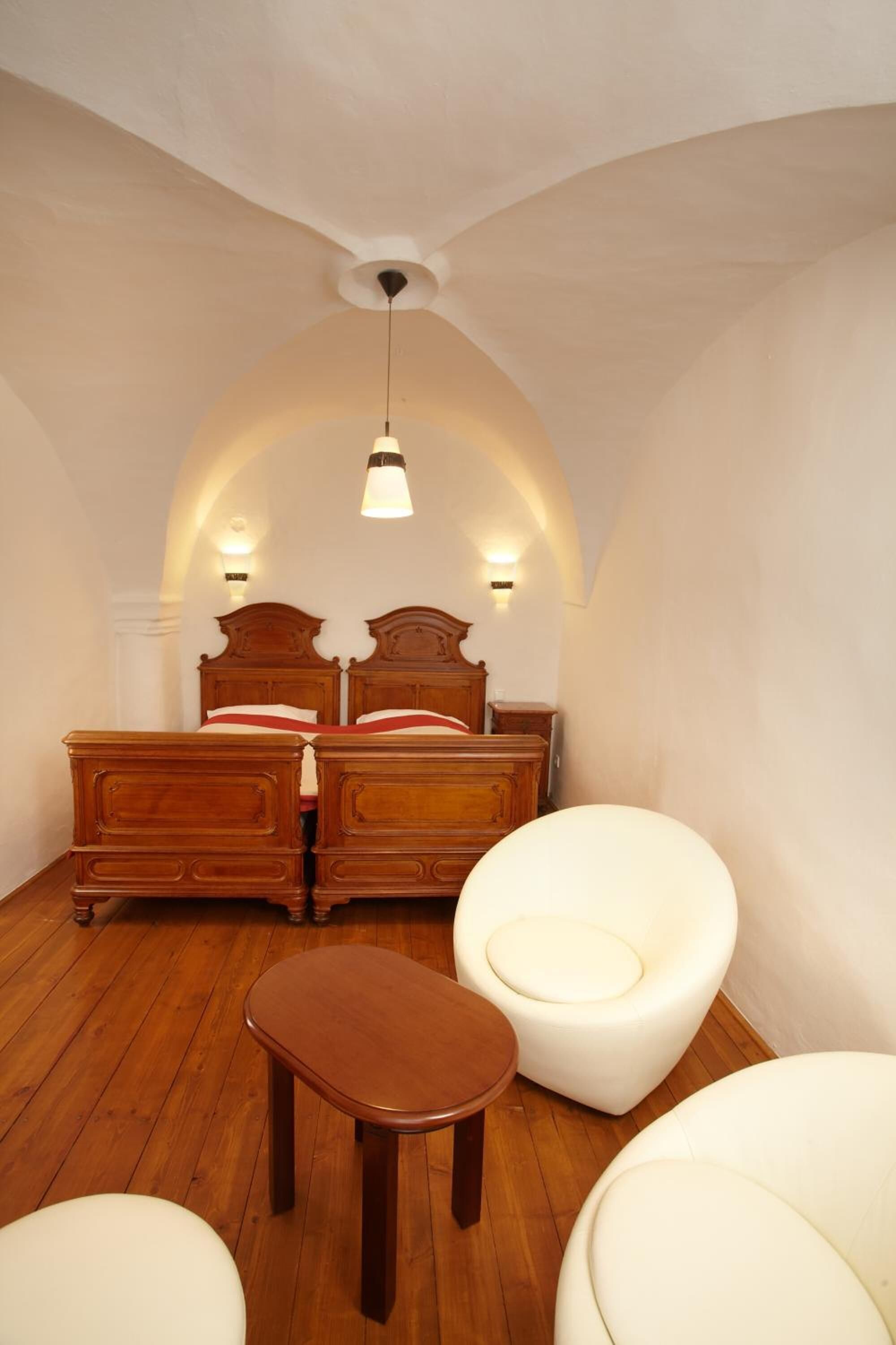 A bedroom with a wooden bed, two bedside tables, a small wooden stool, and two white chairs.