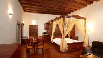 A wooden four-poster bed with a canopy, a dining table with chairs, a desk with a chair, and a small bedside table.