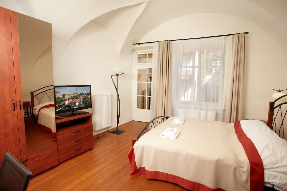 A bedroom with a bed, a wooden dresser, a TV, a radiator, and a window with curtains.