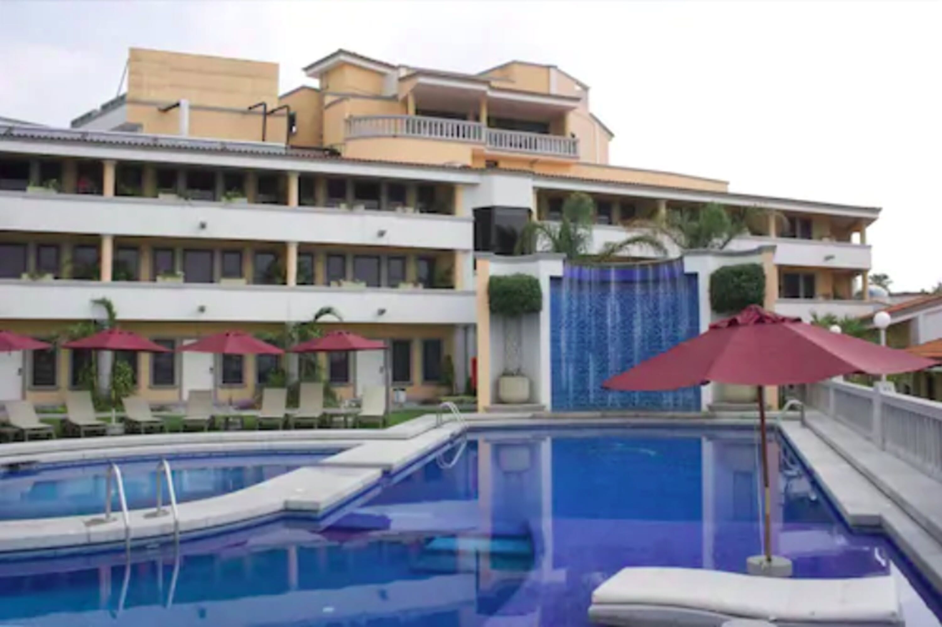 A hotel with a swimming pool, multiple balconies, and outdoor umbrellas.