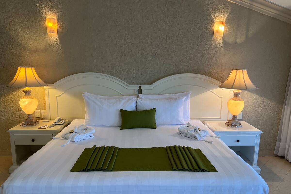 A neatly made bed with white linens, a green throw, and two bedside lamps.