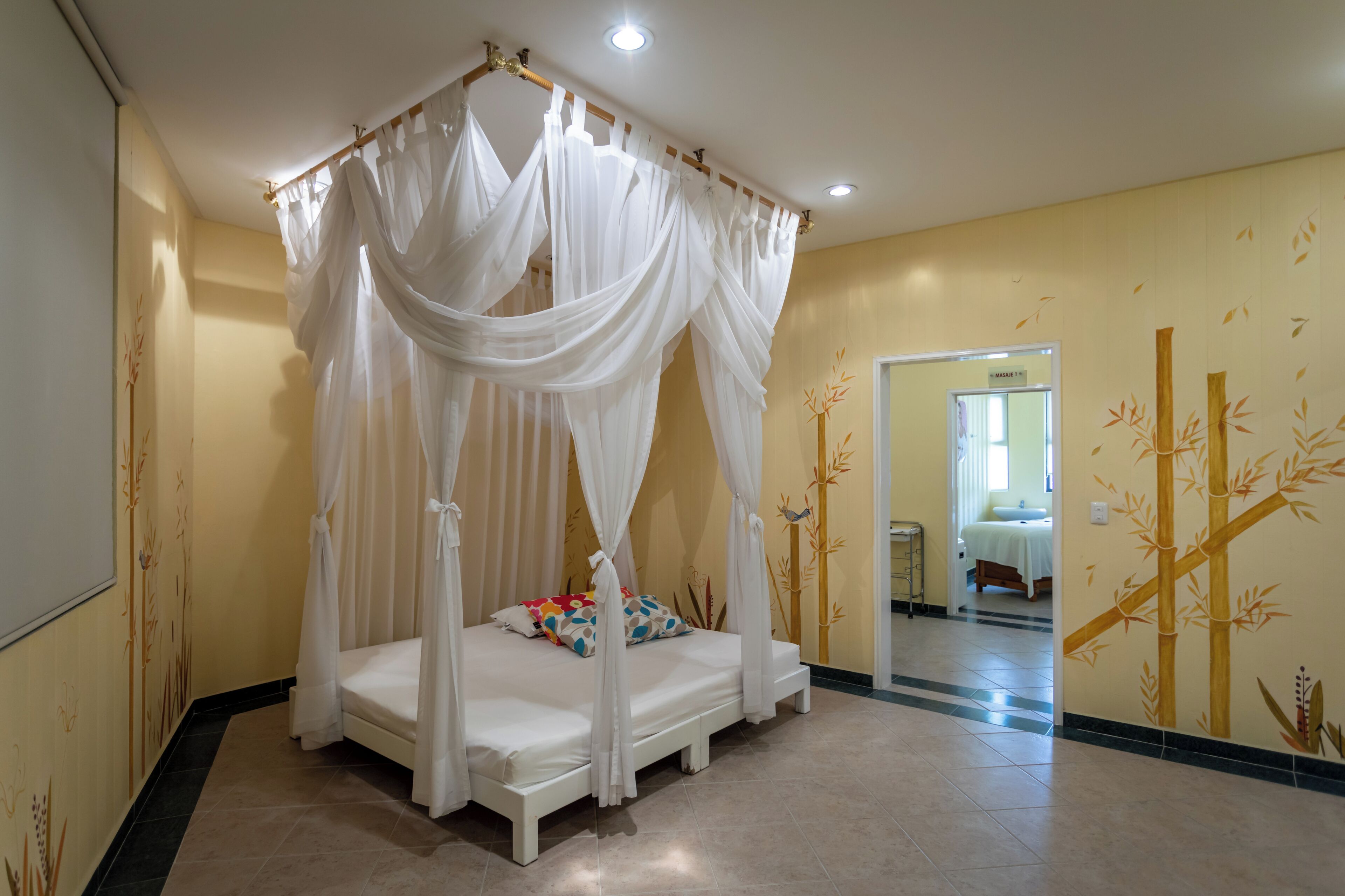 A room with a four-poster bed, a mirror, and a wall with bamboo artwork.