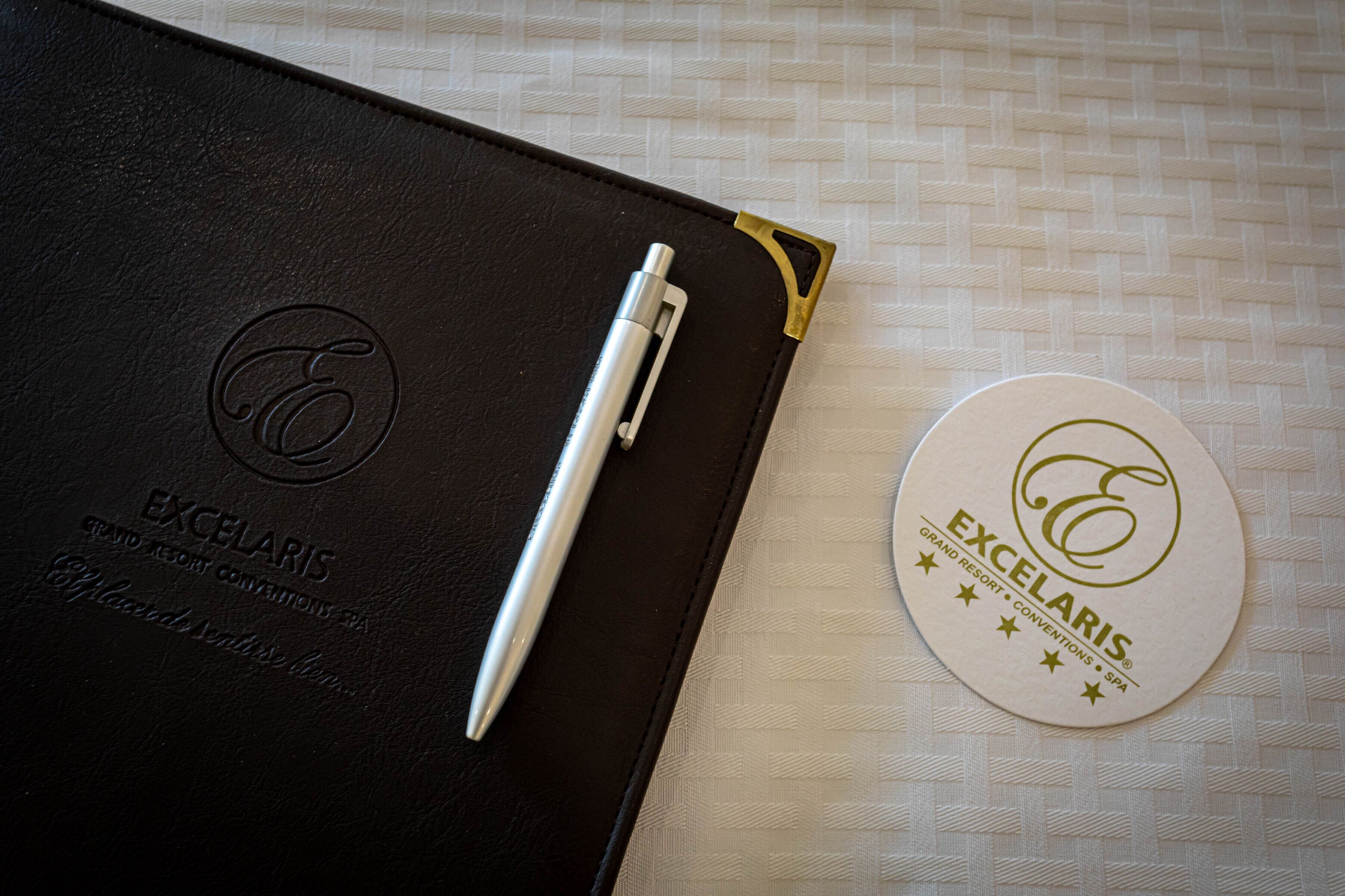 A black leather folder with embossed text and a pen, and a white coaster with embossed text.