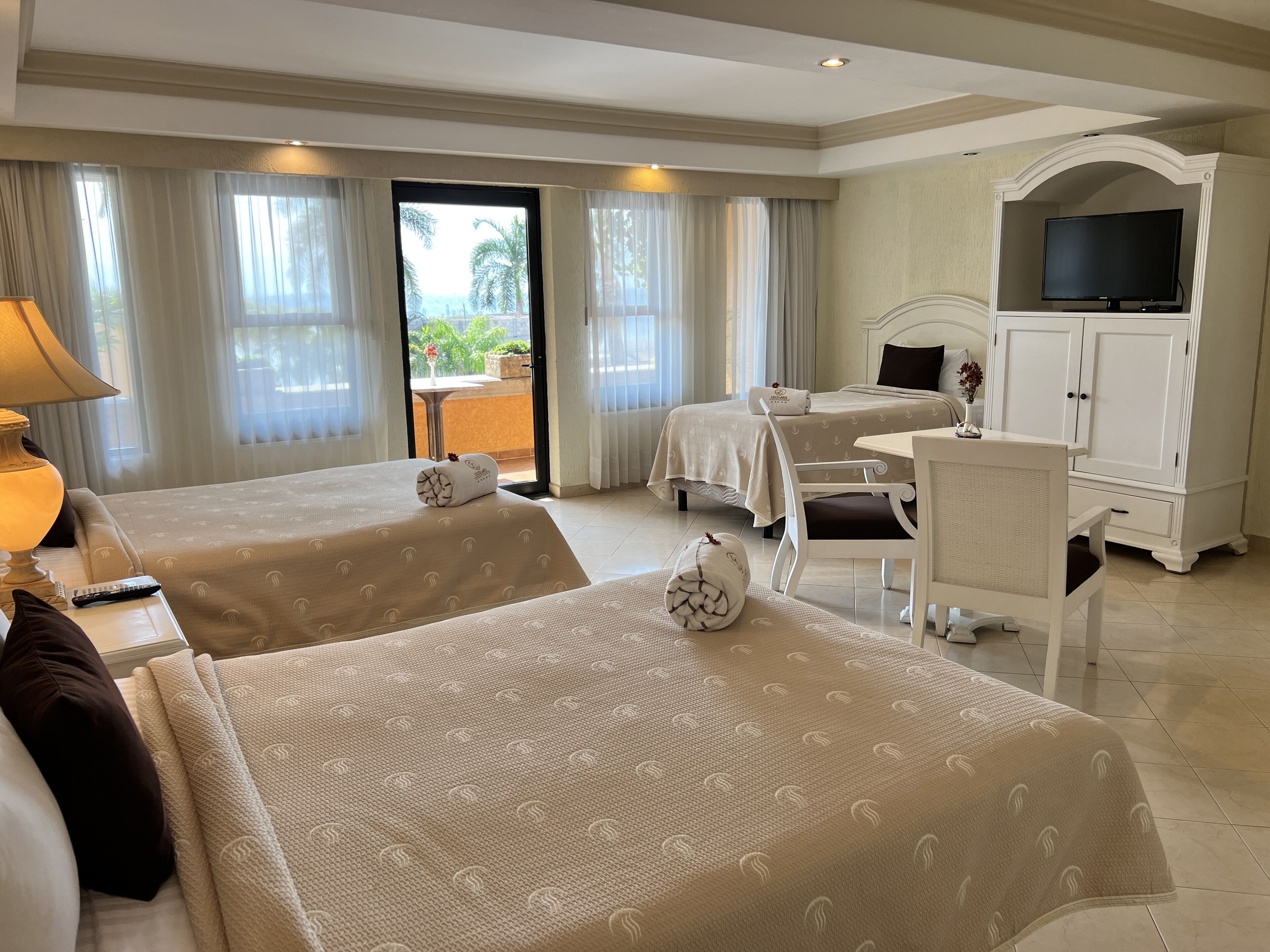 Une chambre d’hôtel avec deux lits, un bureau, une télévision et un balcon avec des rideaux.