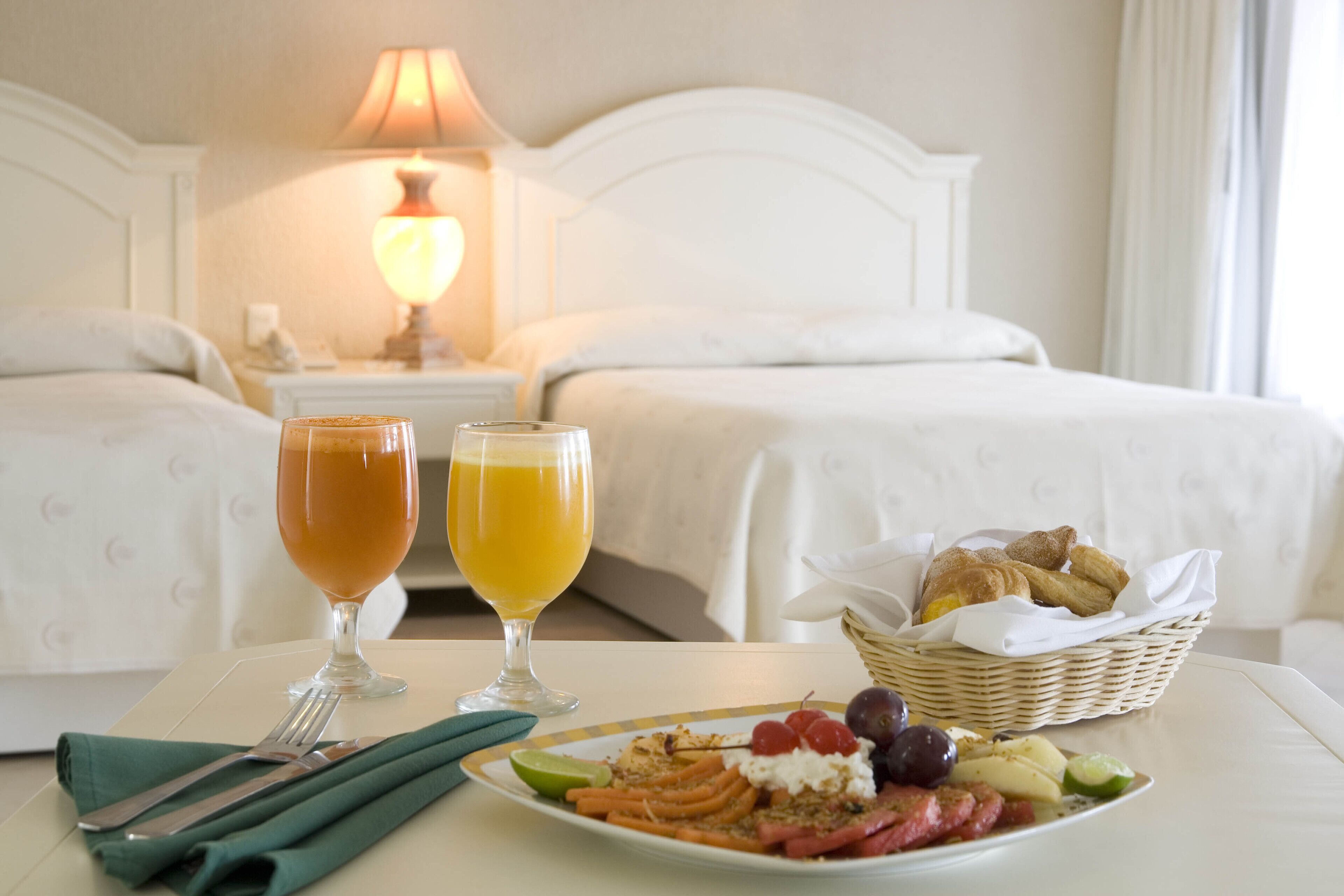 Una mesa en una habitación de hotel con un plato de comida, dos vasos de zumo de naranja y una cesta de bollería.
