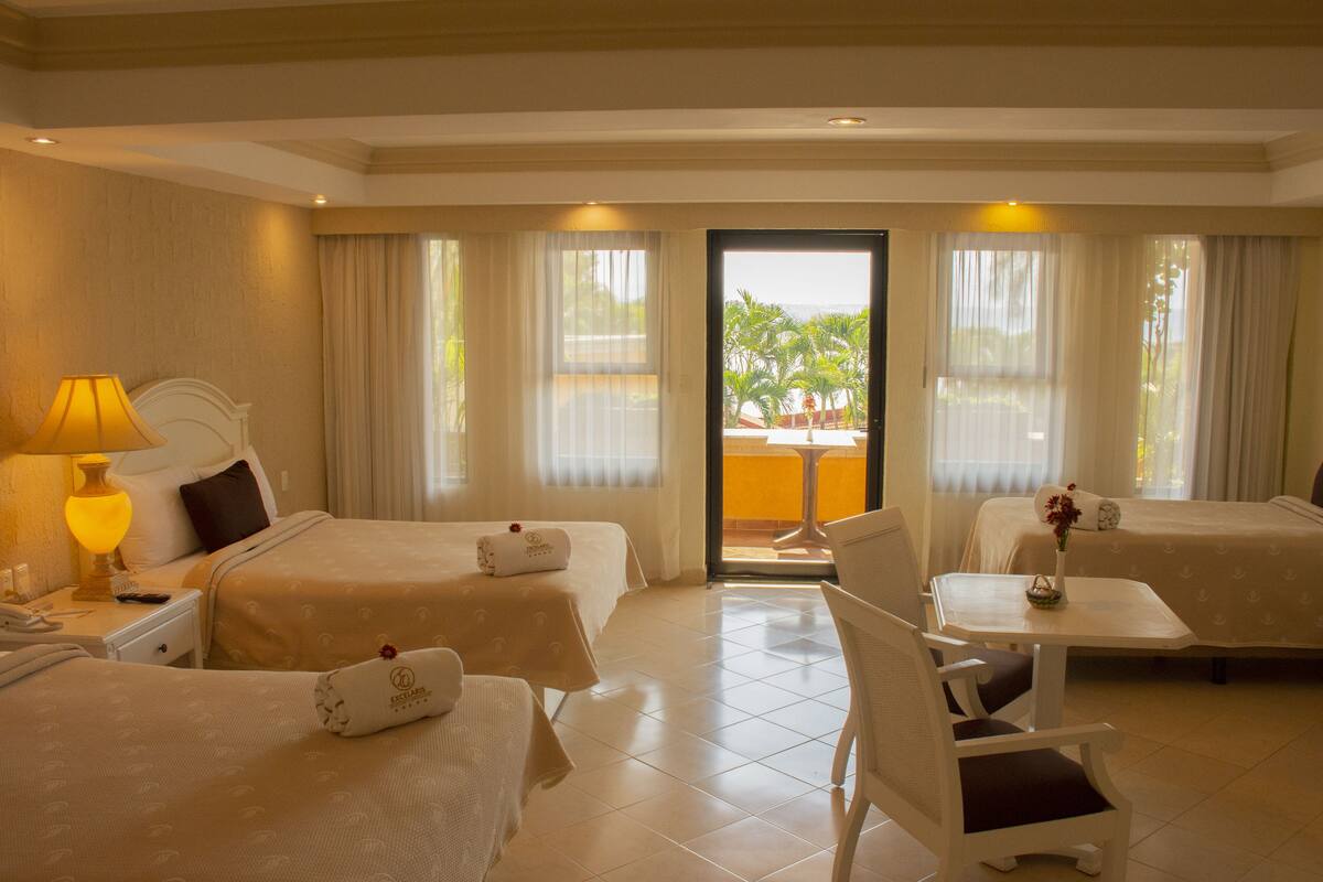 A hotel room with two beds, a small table, a chair, a lamp, and a view of the outdoors.