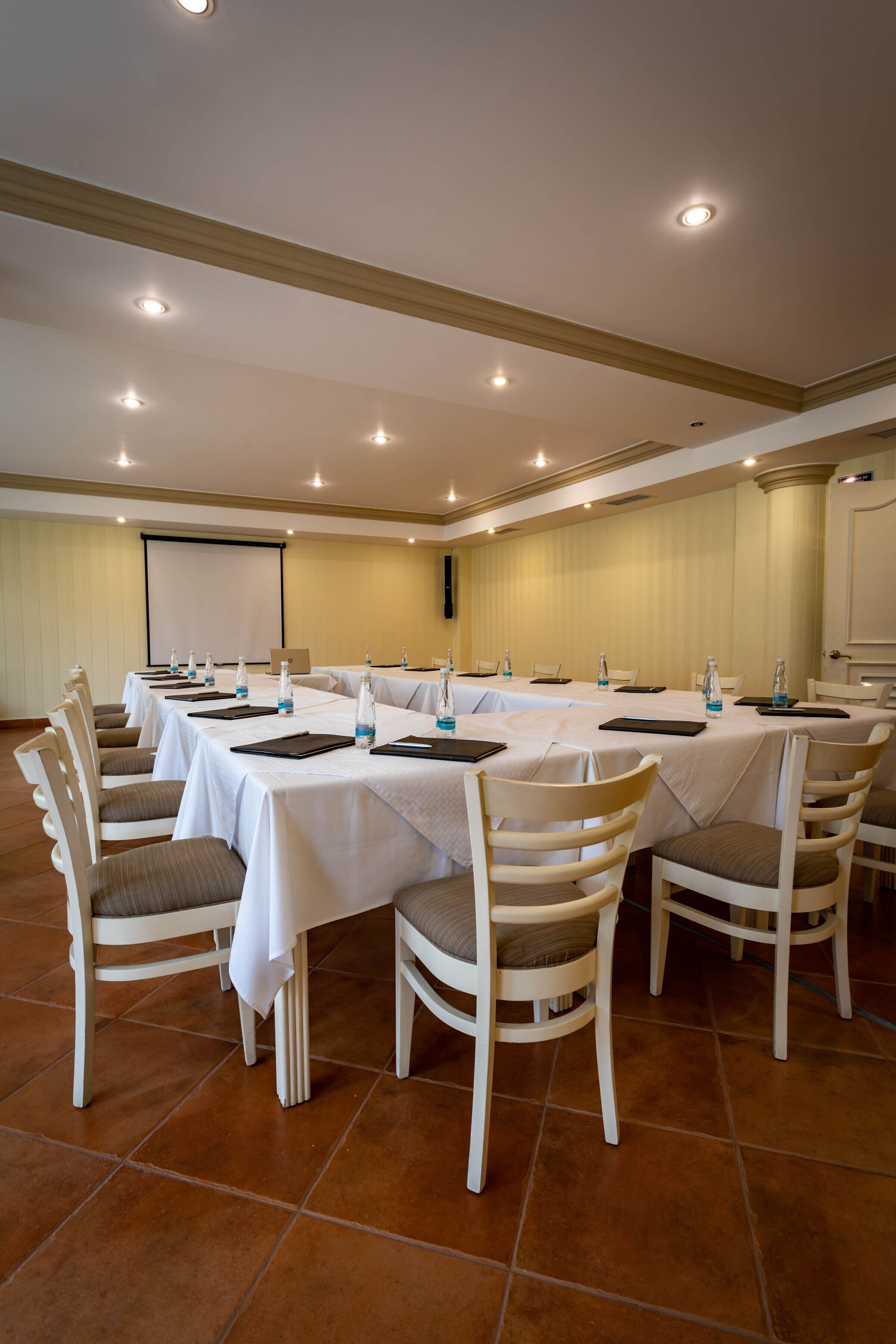 A conference room with multiple tables and chairs, equipped with water bottles and notepads.
