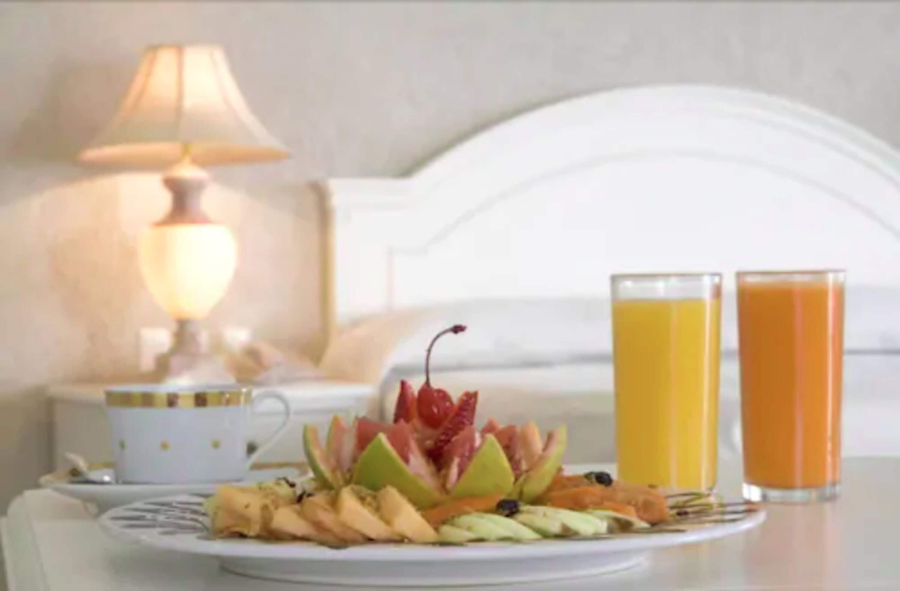 A breakfast setting with a plate of fruit, two glasses of orange juice, and a cup on a table.