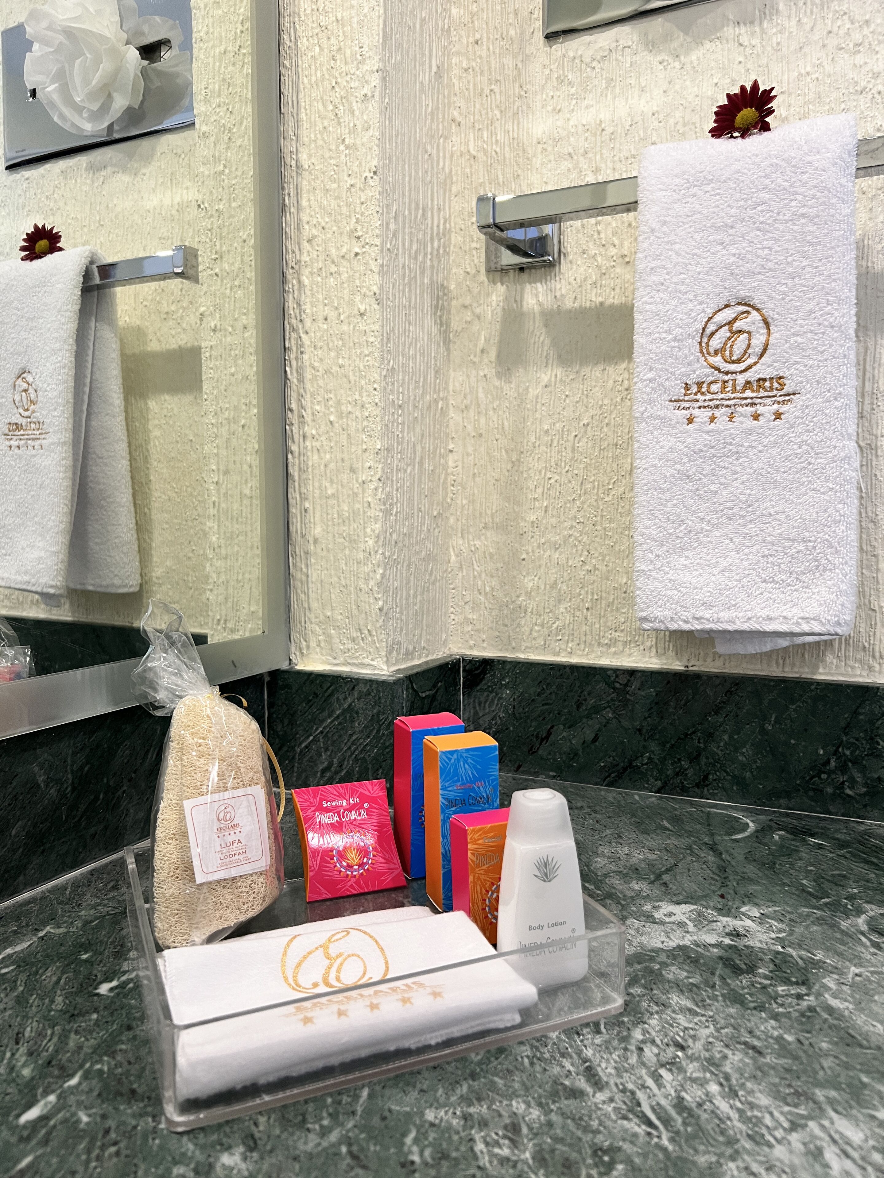 Une salle de bain dotée d’un comptoir en marbre, d’un porte-serviettes avec des serviettes blanches et d’un ensemble de produits de toilette comprenant une lotion pour le corps.