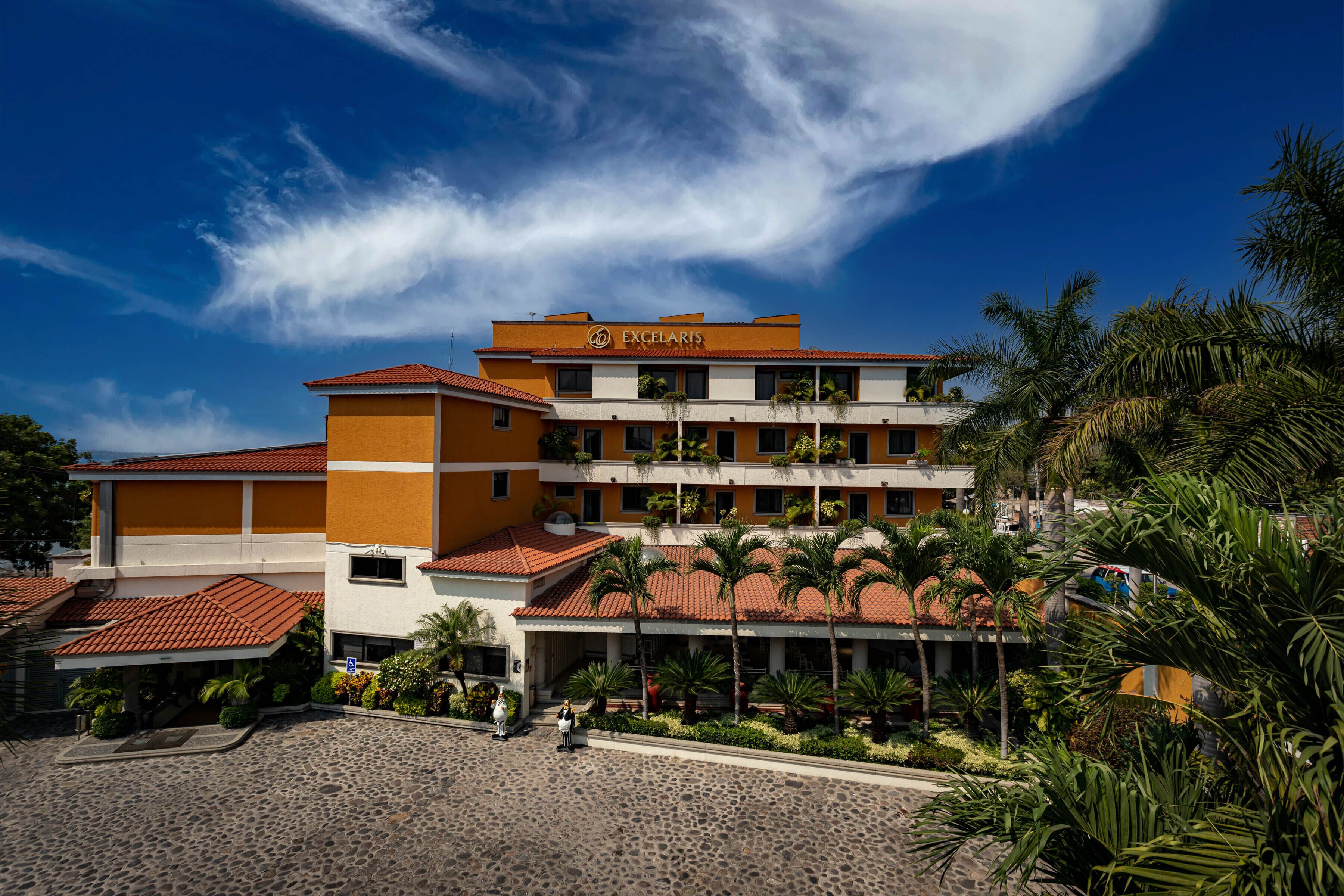 A hotel with multiple floors, a red-tiled roof, and a sign reading "EXCELARIS".