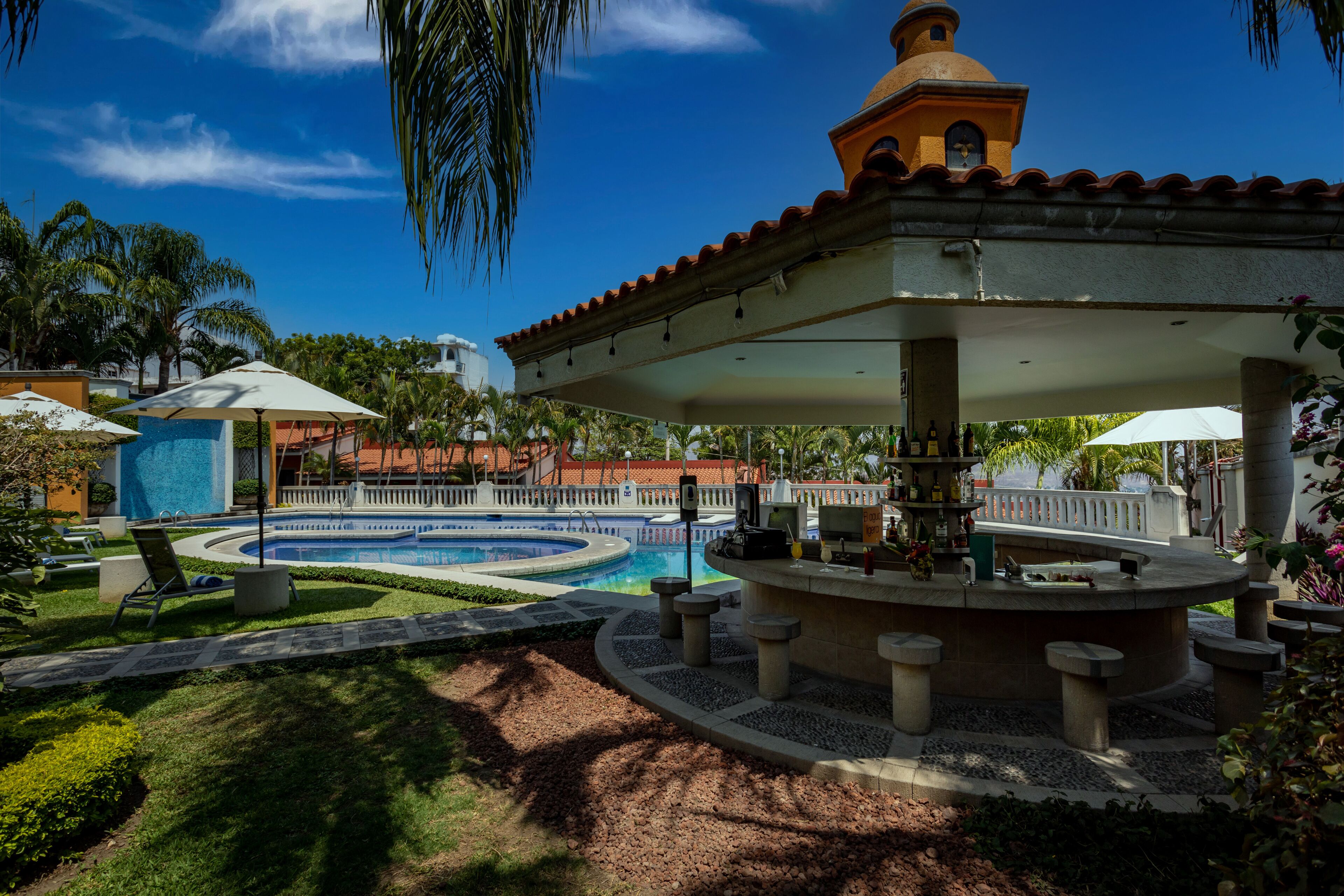 A pool area with a circular fountain, lounge chairs, and a covered seating area with tables.