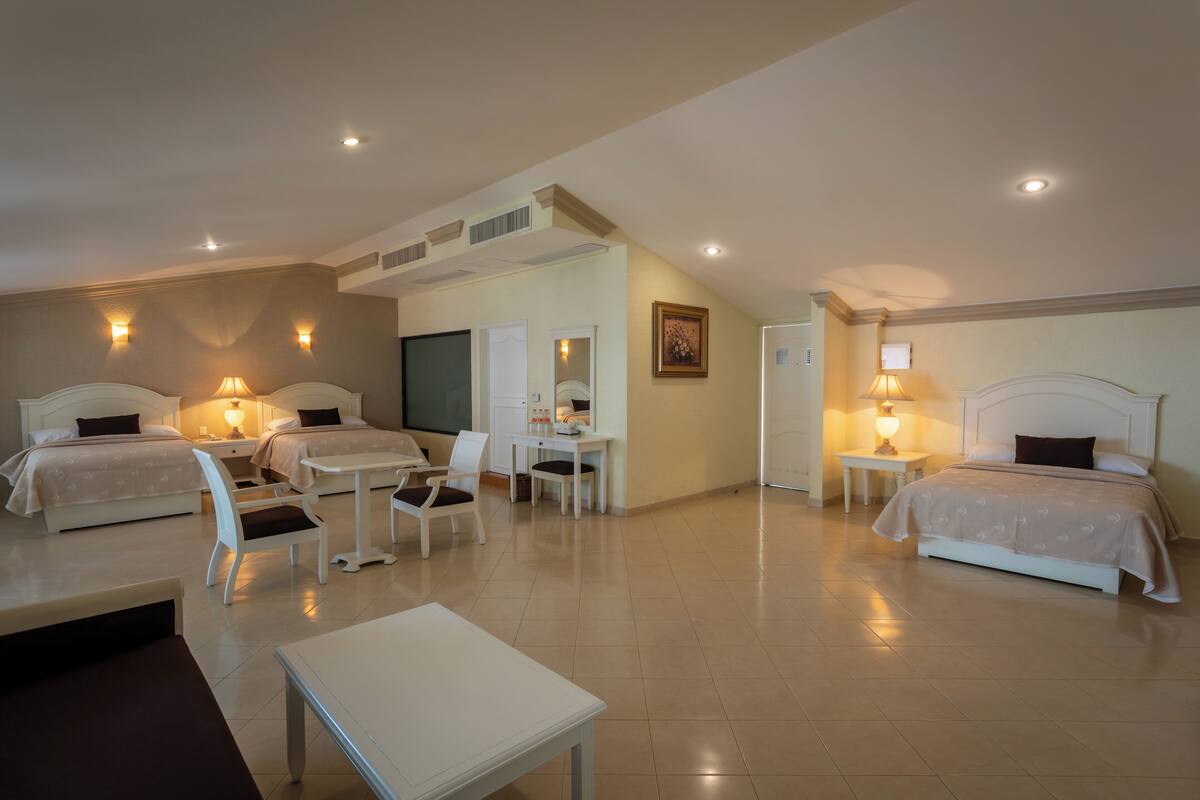 A hotel room with two beds, a desk, a chair, a small table, and a bathroom.