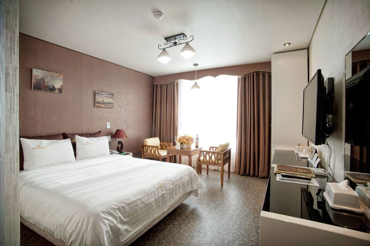Una habitación de hotel con una cama grande, un escritorio con televisor y una ventana con cortinas.