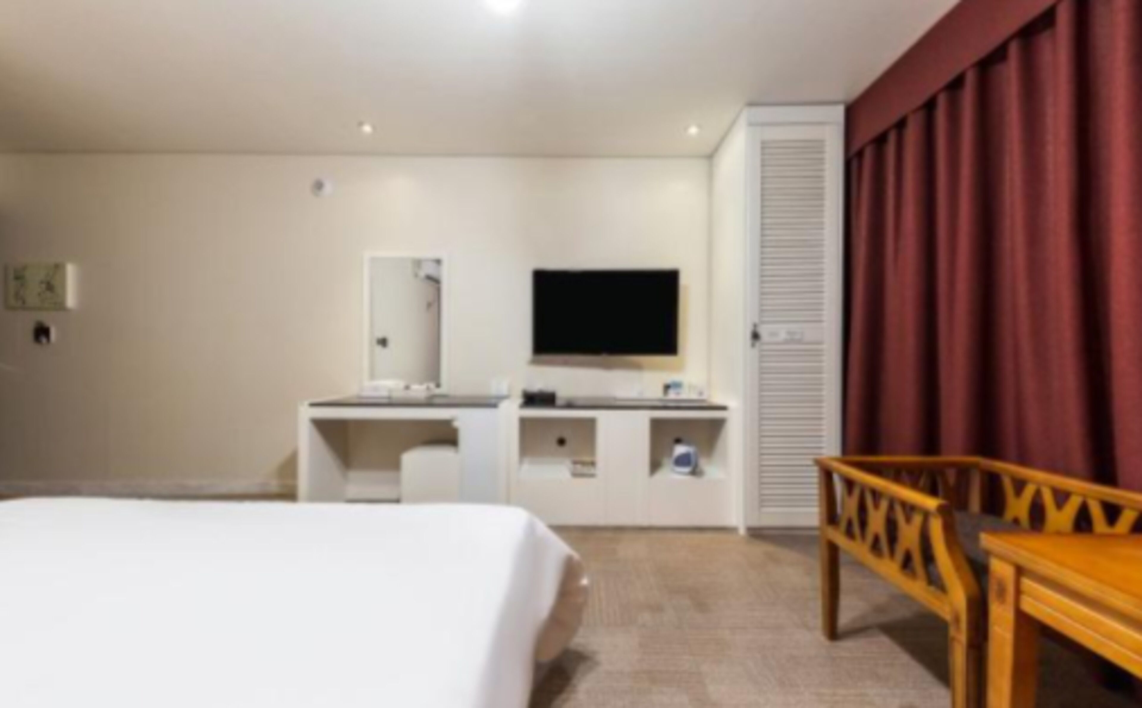 A hotel room with a bed, a desk with a flat-screen TV, a mirror, and a red curtain.