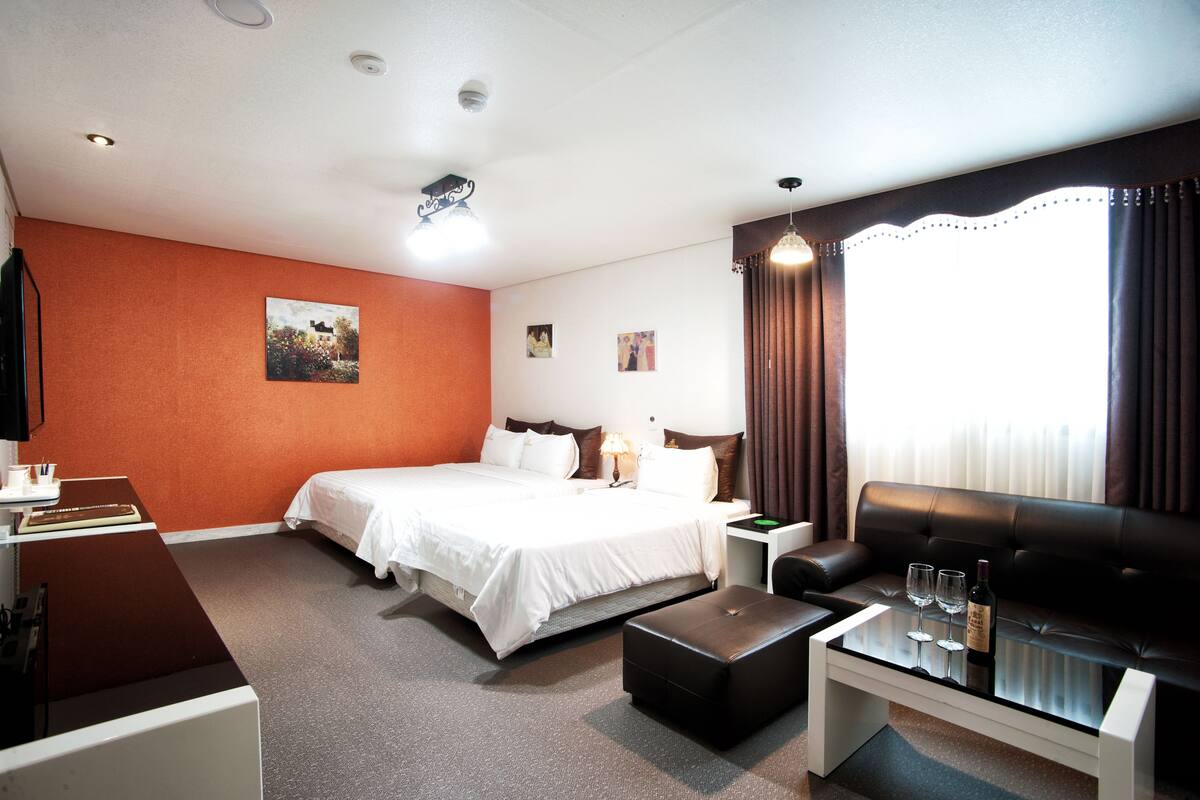 Una habitación de hotel con cama, sofá, una mesa de centro con copas de vino, escritorio y lámpara.
