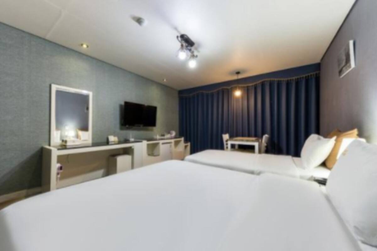 Habitación de hotel con dos camas, un escritorio, un televisor y un ventanal con cortinas.