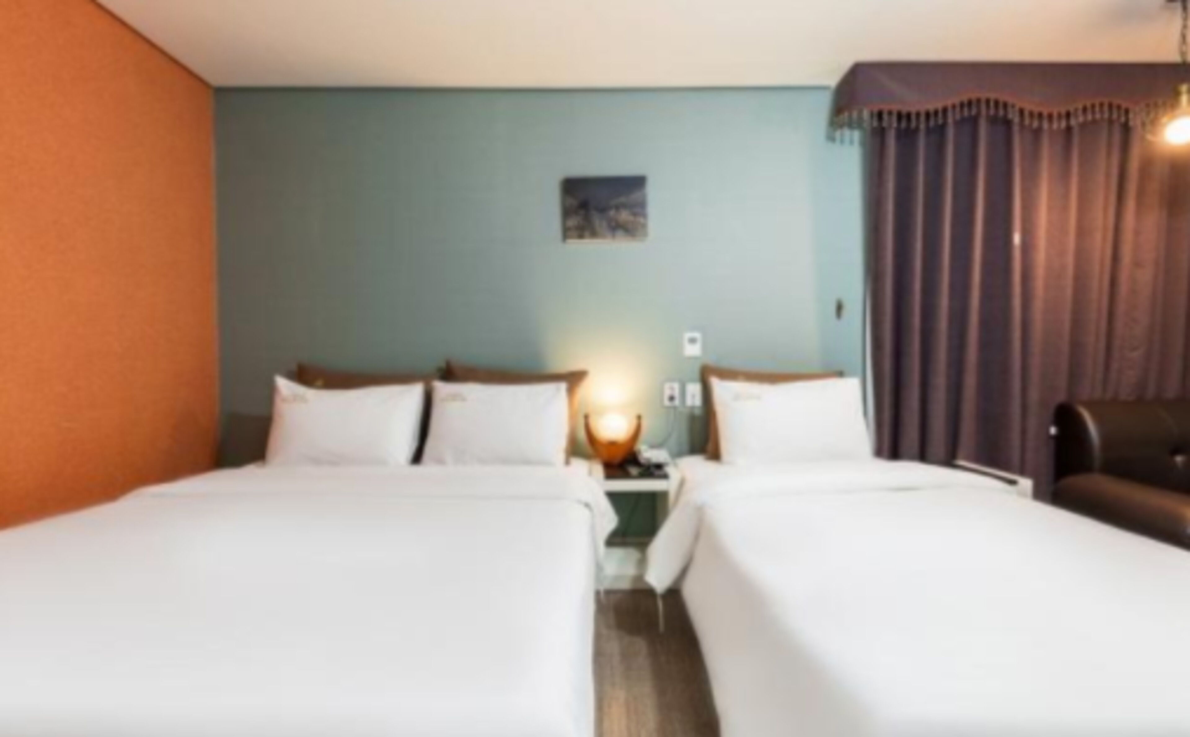 A hotel room with two beds, a nightstand, a lamp, and a painting on the wall.