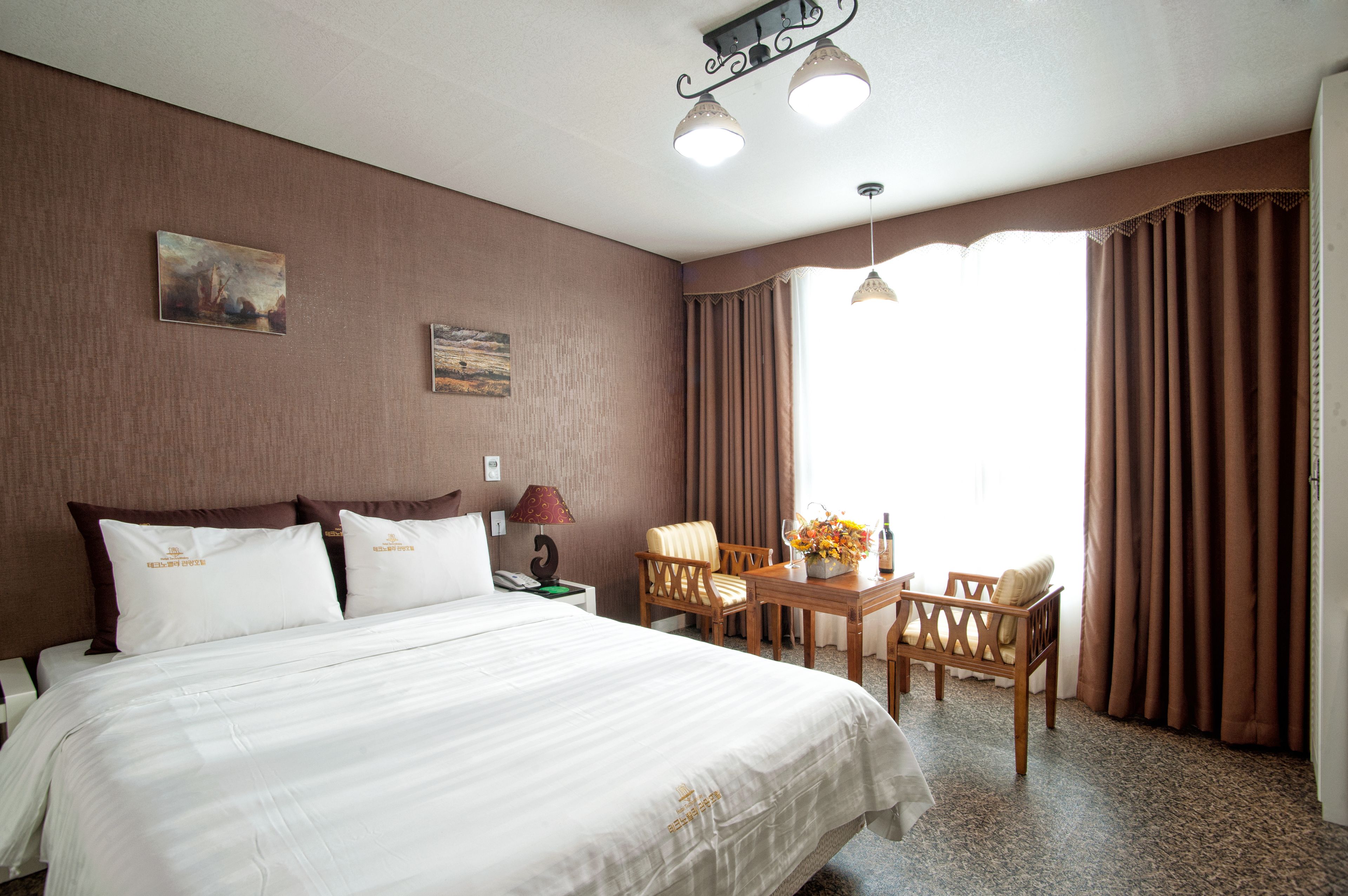 Una habitación de hotel con una cama grande, un escritorio con silla, una lámpara y una ventana con cortinas.