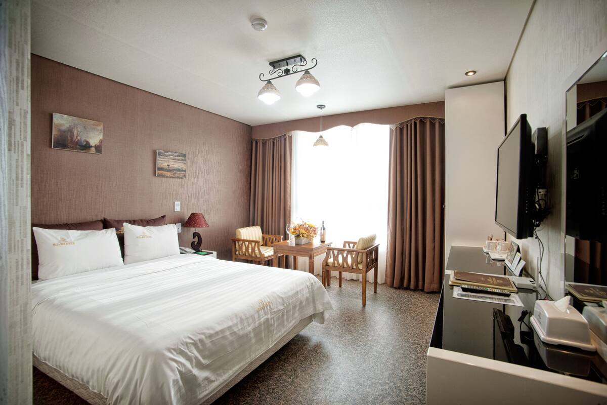 Una habitación de hotel con una cama grande, un escritorio con silla, televisión y una ventana con cortinas.
